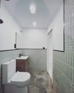 Reforma de baño con wc, lavabo , vista desde plato de ducha, con cerámica gris a media altura moderno e iluminado